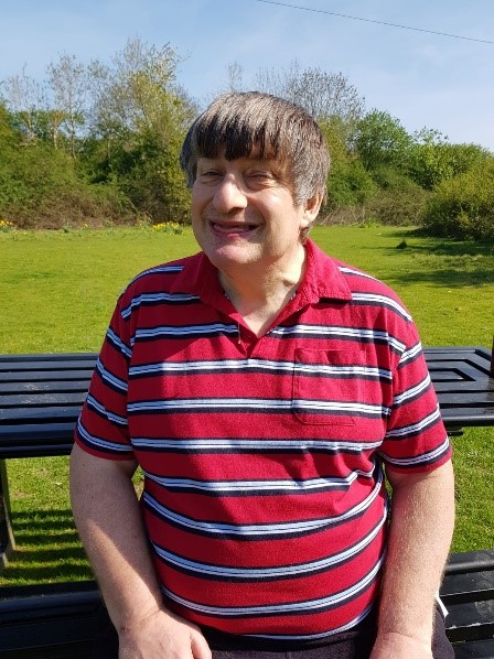 Andrew smiling, sat outside on a bench