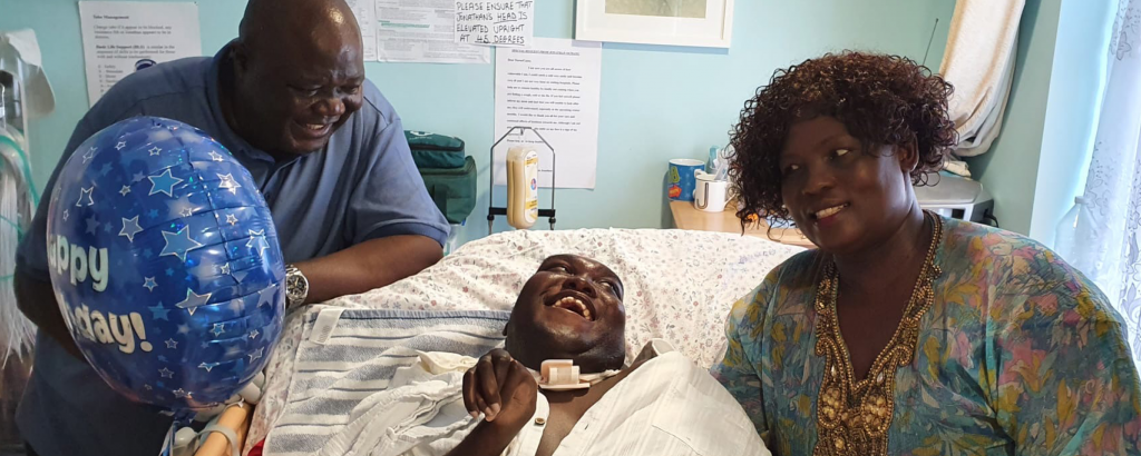 Jonathan is smiling on a hospital bed in between his Dad James on the left and his Mum on the right, who are both looking at and smiling at him.