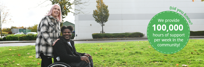 Image of Woman in checked black and white jacket pushing a man in a wheelchair through a park with an industrial unit in the background. 

On the right of the image is a green circle with the words "Did you know?" in green text curved around the outside of the top right.

The text on the circle is white and reads, "We provide 100,000 hours of support per week in the community!"