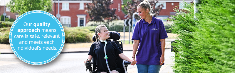 Image of young girl with tracheostomy in a wheelchair, walking with her healthcare assistant in a purple top. They are looking at each other and smiling. On the left is a blue roundal with white text that reads, "our quality approach means care is safe, relevant and meets each individual's needs."